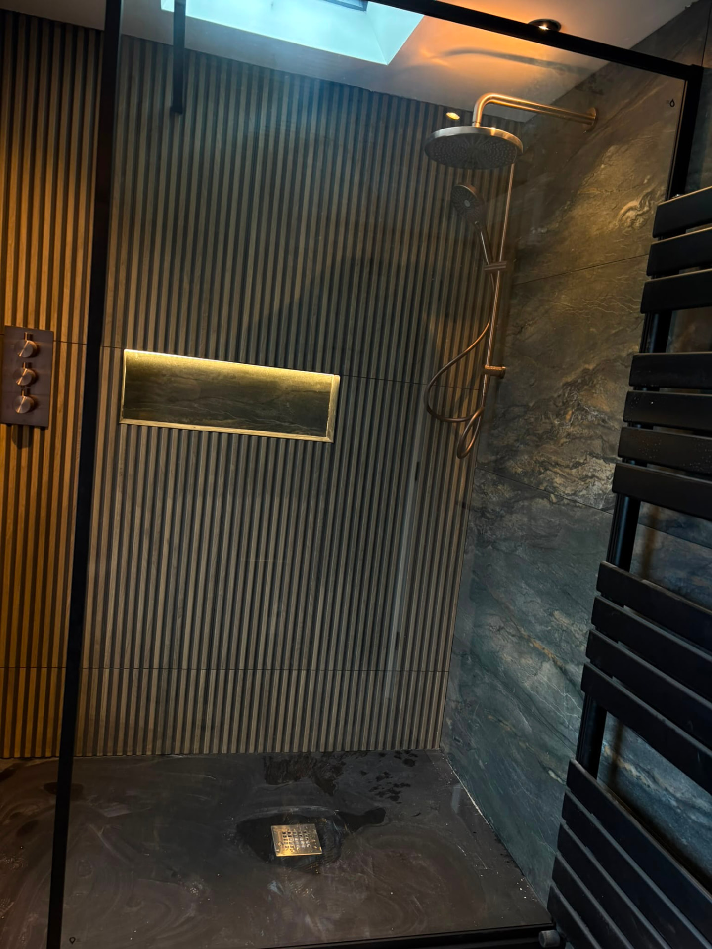 Walk-in wet room with fluted tiling, brushed copper rain shower and lit recessed shelf