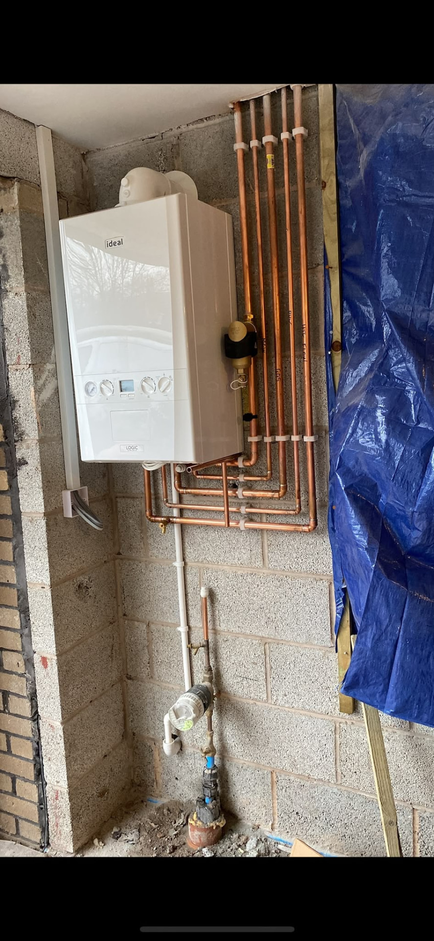 Ideal Logic combi boiler mounted on a garage wall with labelled copper pipework