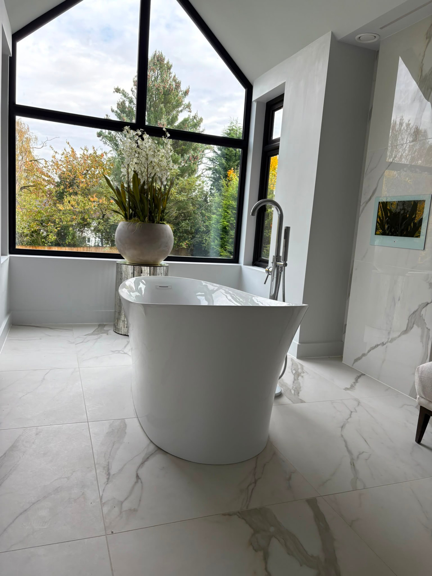 Freestanding bath in a marble tiled bathroom with floor standing bath filler